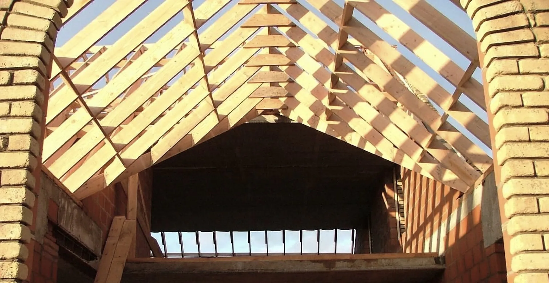 Houten dakstructuur tussen gemetselde gevels, met de zon door de latten
