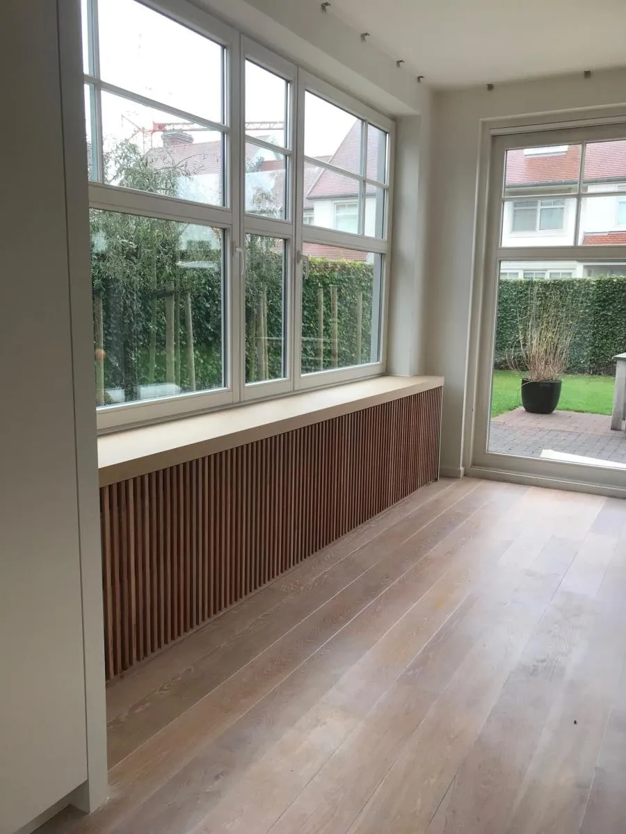 Radiatorkast met houten lamellen onder een raampartij