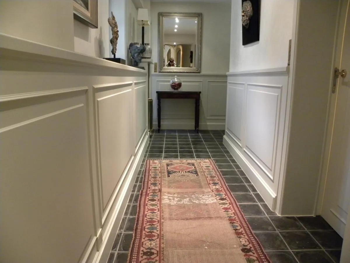 Lange gang met witte wandpanelen en een smalle tapijtloper