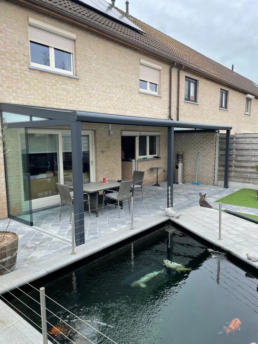 Terras met overkapping langs een woning, met een vijver op de voorgrond